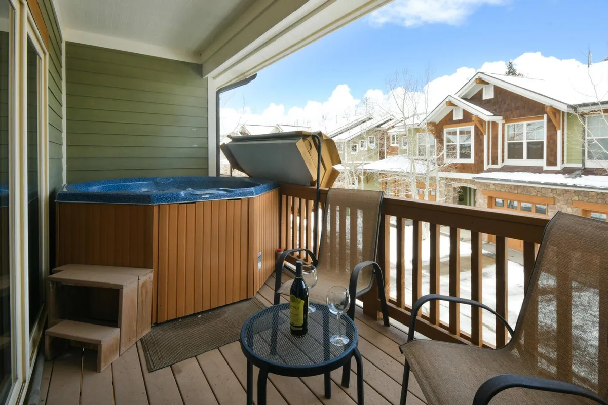 An inviting exterior scene showcasing a luxurious hot tub with people relaxing, surrounded by outdoor seating and wine glasses, set against a colorful sunset sky. The atmosphere suggests unwinding after an active day in the mountains.