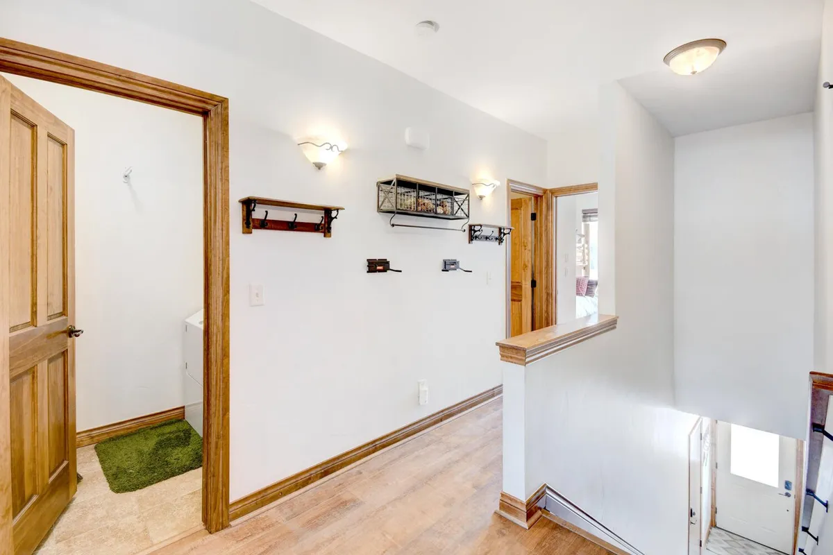 This image captures the condo's entryway, featuring a warm wooden door frame, stylish light fixtures, wall hooks for organizing belongings, and a staircase leading further inside. The mood is welcoming and organized.