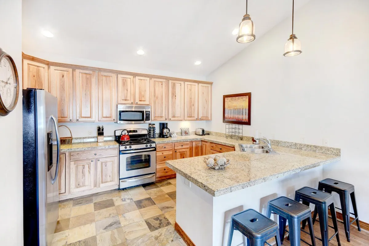 A beautifully appointed kitchen featuring granite countertops, stainless steel appliances, rich wood cabinetry, and bar stools tucked under an inviting breakfast bar. The space is styled for both cooking and casual conversations, with a welcoming, well-lit atmosphere perfect for culinary creativity.