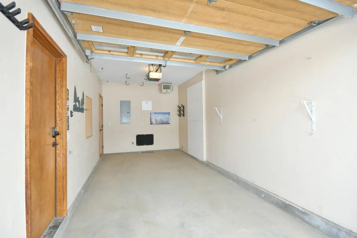 An interior view of the garage with a sturdy wooden door, wall hooks for storing gear, and utility fixtures. The space is tidy and functional, ready to house personal vehicles or outdoor equipment.