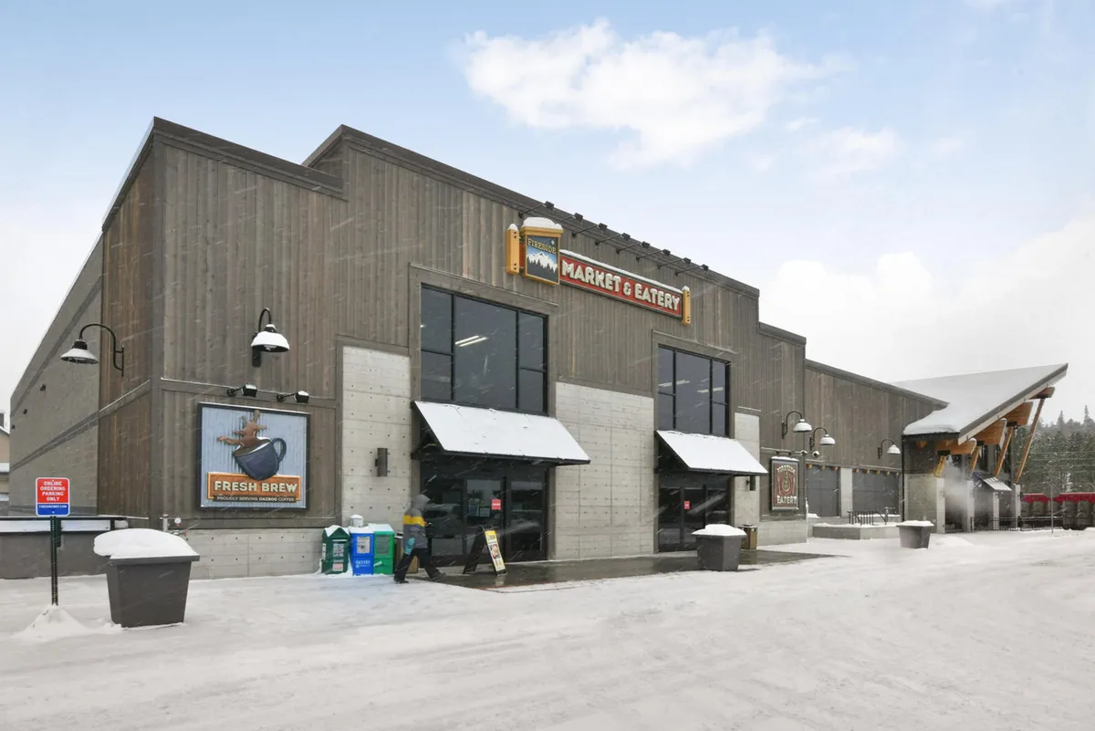 A welcoming exterior of the Fireside Market & Eatery, with inviting signage and snow on the ground, signaling easy access to groceries and snacks right across the street from the condo. The entrance exudes a cozy, communal vibe.