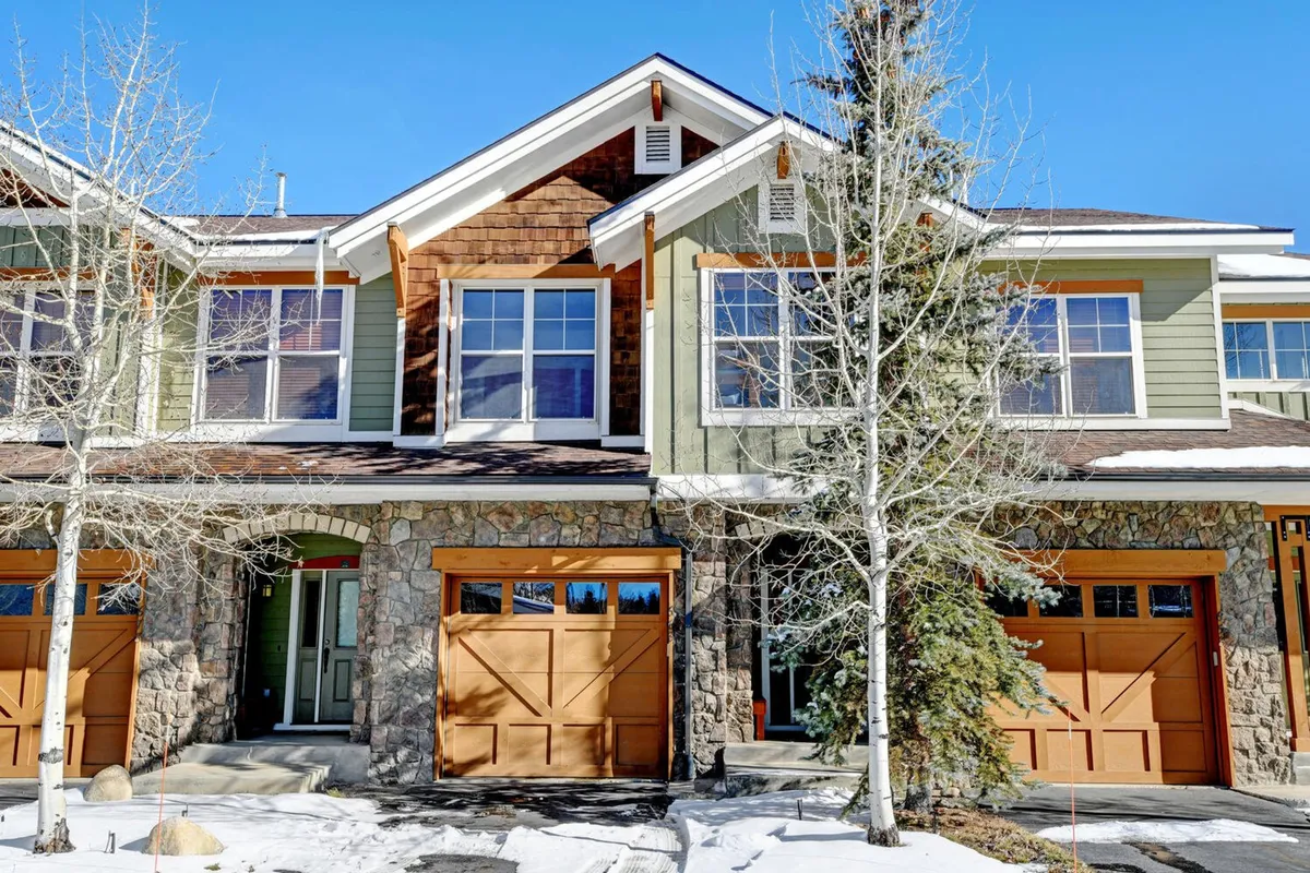 The exterior of a luxury condo building with a handsome stone facade, wooden garage doors, architectural shingles, large windows, and trees framing the property. The setting is inviting, hinting at both privacy and upscale living within a lively neighborhood.