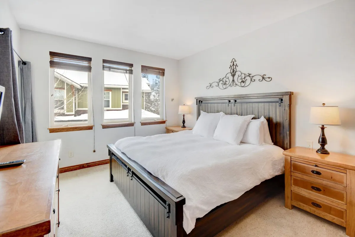 A spacious, sunlit bedroom featuring a large bed with plush bedding, wooden nightstands, and a window offering views of the outdoors. The space is filled with natural light, inviting guests to relax and enjoy the scenery just beyond the glass.
